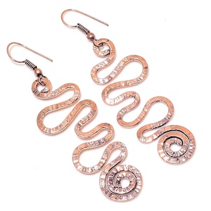 May include: A pair of long, copper earrings with a hammered texture. The earrings are shaped like a series of connected loops and swirls.