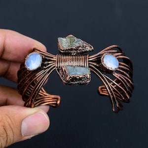 May include: A copper wire bracelet featuring three iridescent stones and a rough, grey stone. The bracelet is woven with copper wire and has a delicate, intricate design.