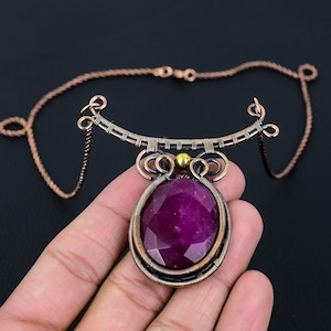 May include: A copper wire wrapped necklace with a large, faceted, purple gemstone pendant. The pendant is accented with a small gold bead.