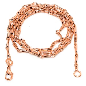 May include: A rose gold chain necklace with a lobster clasp and a jump ring. The chain is made of small, rectangular links.