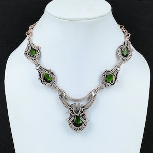 May include: A silver wire wrapped necklace with green gemstone accents. The necklace features a teardrop-shaped pendant with a larger green gemstone.
