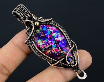 Pode incluir: Um pingente envolto em fio de cobre com uma pedra oval colorida e iridescente com um padrão roxo, azul, rosa e verde. O pingente tem uma pequena conta dourada na parte superior e uma pequena pedra roxa na parte inferior.