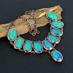 Puede incluir: Un collar de cadena de cobre con un colgante y siete piedras ovaladas de vidrio azul verdoso iridiscente.