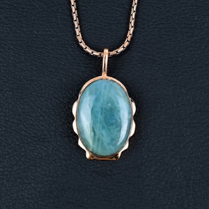 Puede incluir: Un collar de cadena de plata con un colgante de oro rosa con una piedra ovalada azul claro.