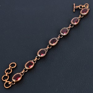 Könnte beinhalten: Ein Kupferarmband mit einem Kettenglieddesign und roten ovalen Edelsteinen.