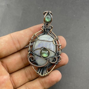 May include: A silver and copper wire wrapped pendant featuring a large oval moonstone and a smaller green labradorite stone.