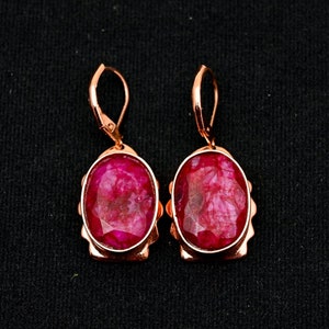 May include: A pair of rose gold earrings with oval-shaped red gemstone settings.