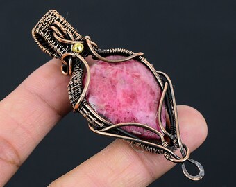 May include: A pink and white gemstone pendant wrapped in copper wire with a gold bead accent. The pendant is hanging from a copper wire loop.