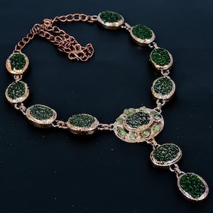 May include: A copper-toned necklace featuring oval-shaped, dark green druzy stones. The stones are set in a copper-colored metal and connected by a delicate chain. The necklace has a pendant with a cluster of smaller green stones.