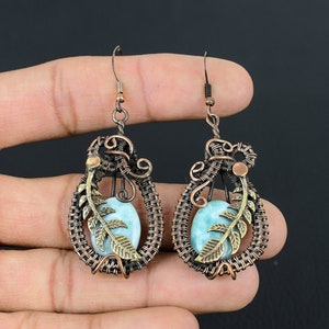 May include: A pair of copper wire wrapped earrings with a blue-green gemstone and a gold leaf design.