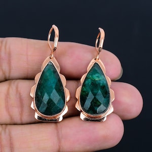 May include: A pair of dangle earrings with a teardrop-shaped green gemstone set in a rose gold setting. The earrings have a scalloped edge.