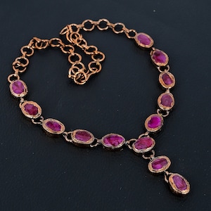 Peut inclure: Un collier en cuivre avec une chaîne et un pendentif orné d'un groupe de pierres précieuses ovales de couleur rose foncé.
