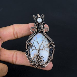 May include: A copper wire wrapped pendant featuring a white moonstone with a tree of life design. The pendant has a small pearl accent at the top.