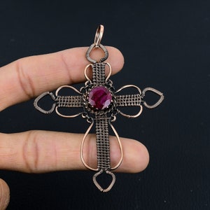 May include: A copper wire wrapped cross pendant with a red gemstone in the center.