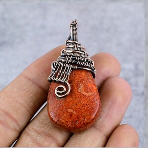 May include: A copper wire wrapped pendant with a red coral stone. The pendant has a spiral design and is wrapped in copper wire.