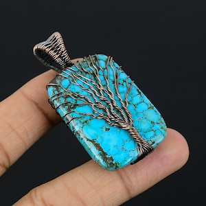 Puede incluir: Colgante rectangular de turquesa con un diseño de árbol de alambre de cobre. La piedra turquesa es de un azul vibrante con vetas marrones. El alambre de cobre está intrincadamente tejido para formar las ramas y el tronco del árbol.