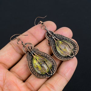 May include: A pair of copper wire wrapped earrings with green and gold teardrop shaped stones.