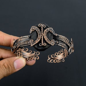 May include: A copper wire bracelet with a black wooden center piece. The bracelet is made of intricate wirework and has a delicate, ornate design.