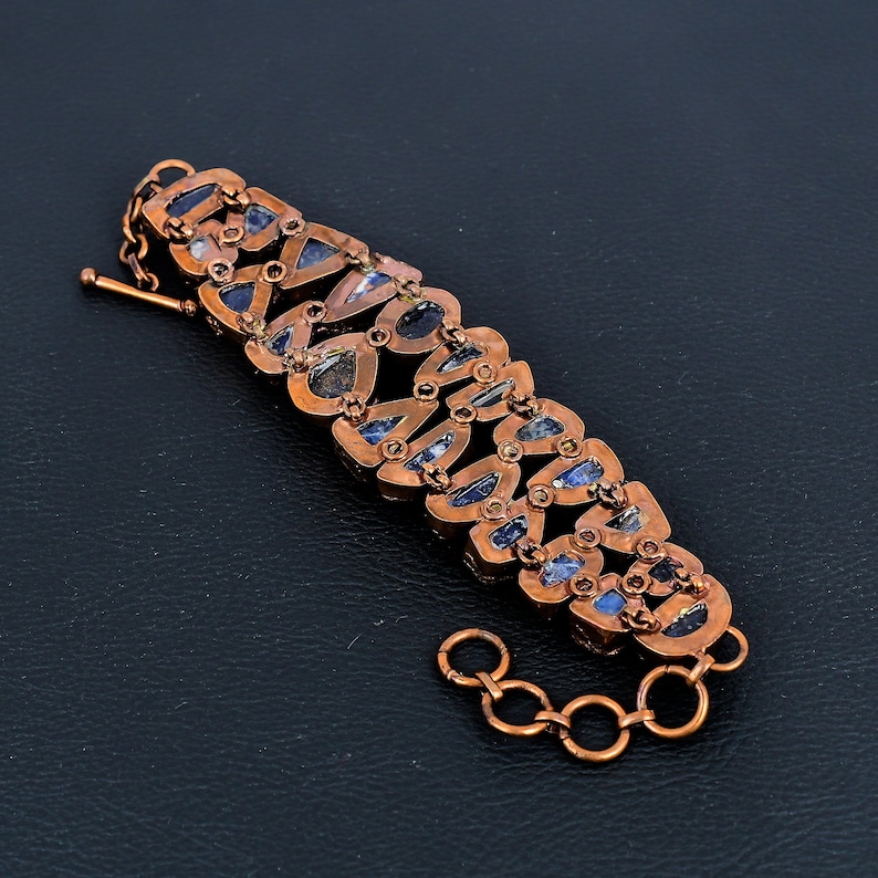 K&ouml;nnte beinhalten: Ein Kupferarmband mit einem Kettenverschluss. Das Armband ist mit einer Reihe von blau-grauen, edelsteinartigen Akzenten verziert.