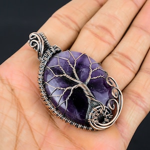 May include: A purple amethyst gemstone tree of life pendant with copper wire wrapping. The pendant is oval shaped and has a detailed wire design.