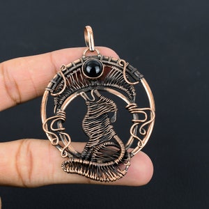 May include: A copper wire wrapped pendant featuring a wolf howling at the moon with a black gemstone in the center.