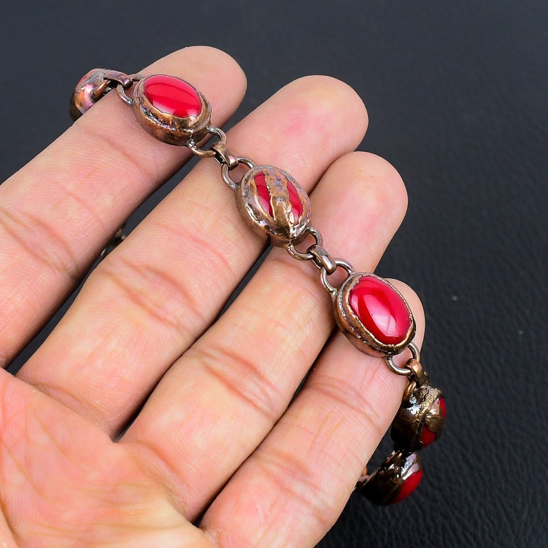 K&ouml;nnte beinhalten: Ein Kupferarmband mit roten ovalen Steinen. Das Armband hat eine strukturierte Oberfl&auml;che und ist aus Metall.