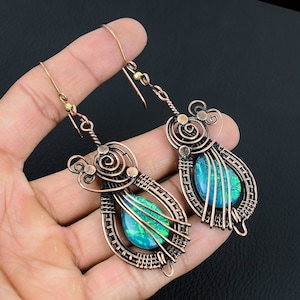 May include: A pair of copper wire wrapped earrings with a green and blue iridescent opal stone in each earring.