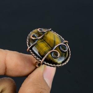 May include: A copper wire wrapped ring with a tiger's eye gemstone. The ring features a delicate, swirling wire design.