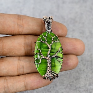 May include: A green glass tree of life pendant with copper wire wrapped around it. The pendant is oval shaped and has a copper bail.