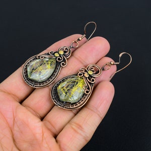 May include: A pair of copper wire wrapped earrings with teardrop shaped green and gold stones.