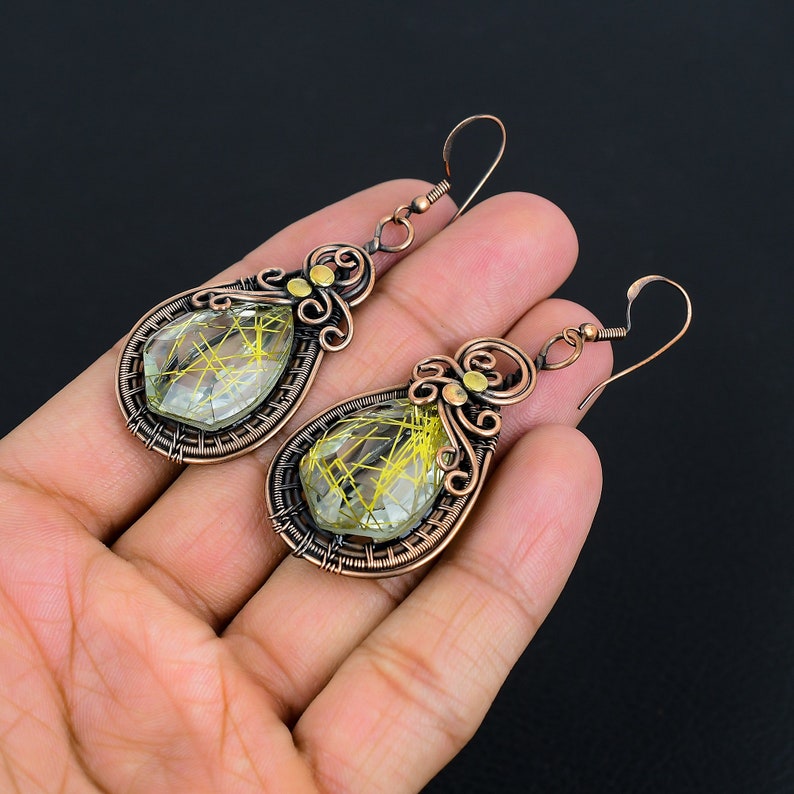May include: A pair of copper wire wrapped earrings with teardrop shaped green and gold stones.