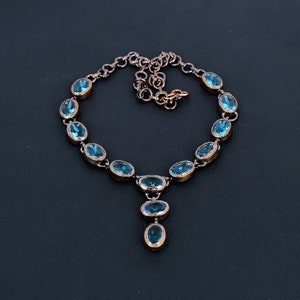 May include: A copper necklace with a pendant featuring a cluster of oval-shaped blue gemstones. The necklace has a chain with a lobster clasp.
