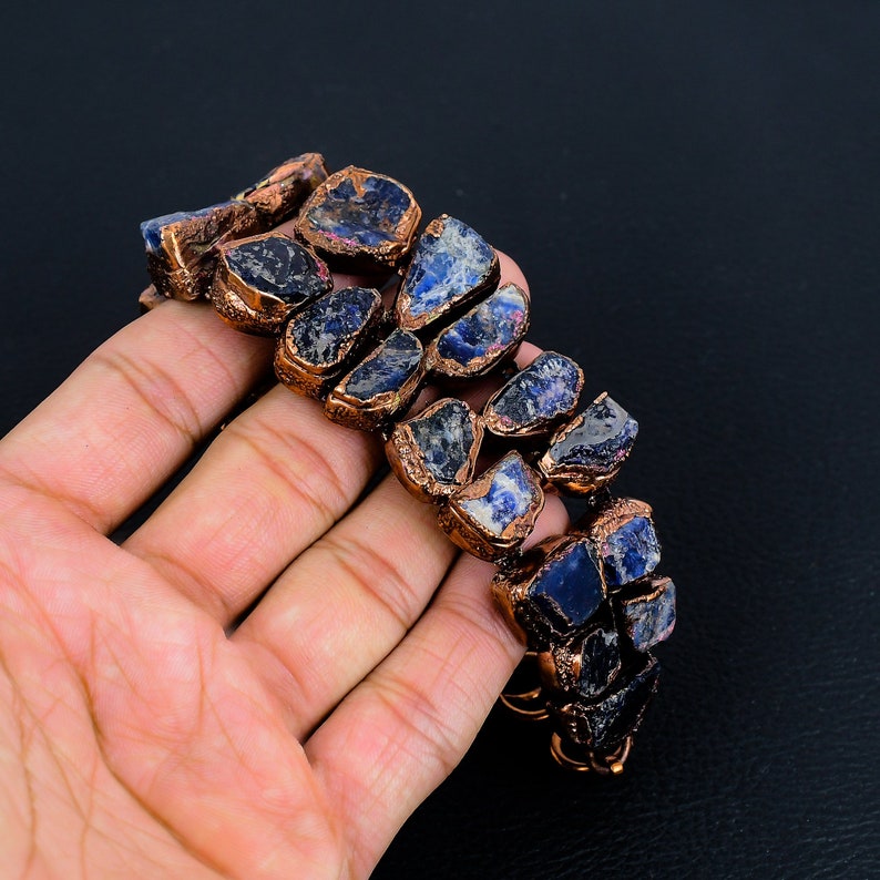 K&ouml;nnte beinhalten: Ein mit Kupferdraht umwickeltes Armband mit blauen und schwarzen Edelsteinen. Das Armband besteht aus nat&uuml;rlichen Steinen und Kupferdraht.