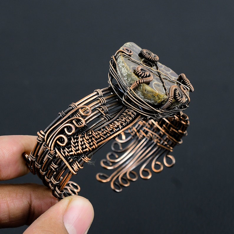 May include: A copper wire wrapped bracelet featuring a brown and grey stone set in the centre. The stone is surrounded by copper wire spirals.
