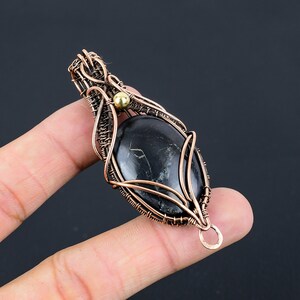 May include: A black gemstone pendant with copper wire wrapping and a gold accent. The pendant is oval shaped and has a delicate design.