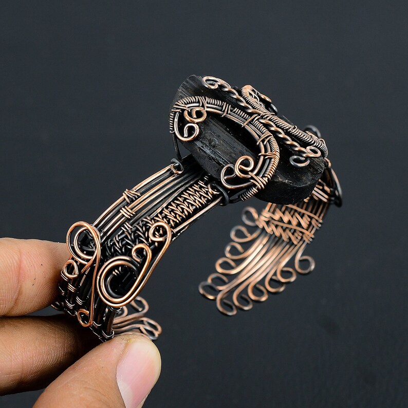 May include: A copper wire wrapped bracelet with a black gemstone. The wire is woven into a intricate design with swirls and loops.