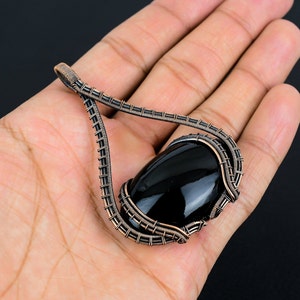 May include: A black gemstone pendant with a copper wire wrap. The pendant is shaped like a teardrop and has a smooth, polished finish.