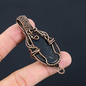 May include: A black gemstone pendant wrapped in copper wire. The wire is woven into a intricate design with a bail at the top.