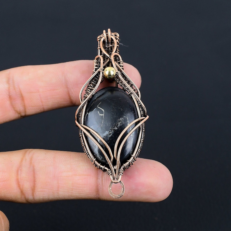 May include: A black gemstone pendant with copper wire wrapping. The pendant has a gold bead at the top and a copper loop at the bottom.