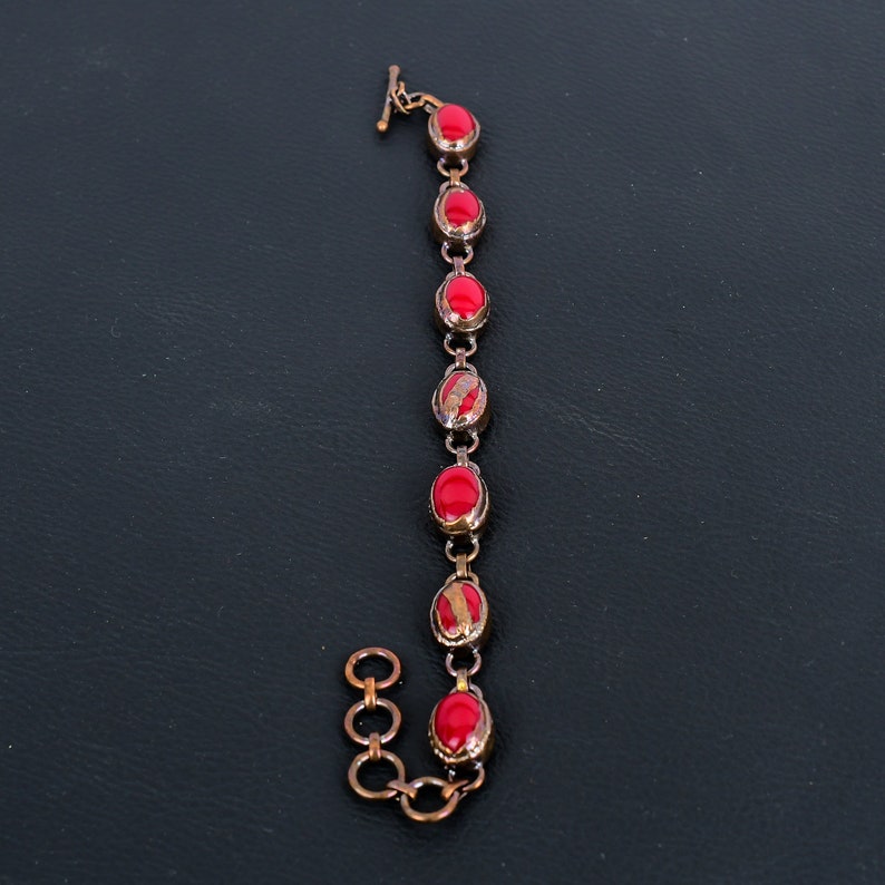 K&ouml;nnte beinhalten: Ein Kupferarmband mit einem Kettenglieddesign und roten ovalen Steinen.