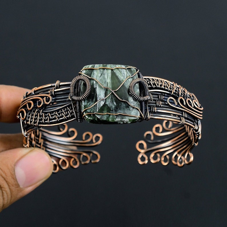 May include: A copper wire wrapped bracelet with a green and black gemstone in the center.