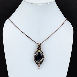 May include: A black gemstone pendant necklace with a copper wire design and a gold bead accent. The necklace has a delicate chain.