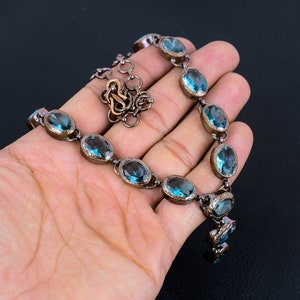 May include: A necklace with a silver chain and oval-shaped blue gemstones. The necklace has a pendant with three smaller blue gemstones.