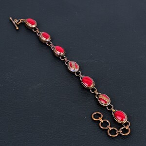 K&ouml;nnte beinhalten: Ein Kupferarmband mit roten ovalen Steinen. Das Armband hat einen Karabinerverschluss.