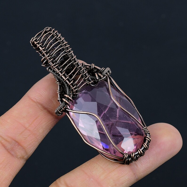 May include: A purple gemstone pendant wrapped in copper wire. The pendant is oval shaped and has a faceted design.