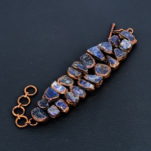 K&ouml;nnte beinhalten: Ein Kupferarmband mit einer Reihe unregelm&auml;&szlig;iger, dunkelblauer und violetter Edelsteine. Das Armband hat einen Kupferverschluss.