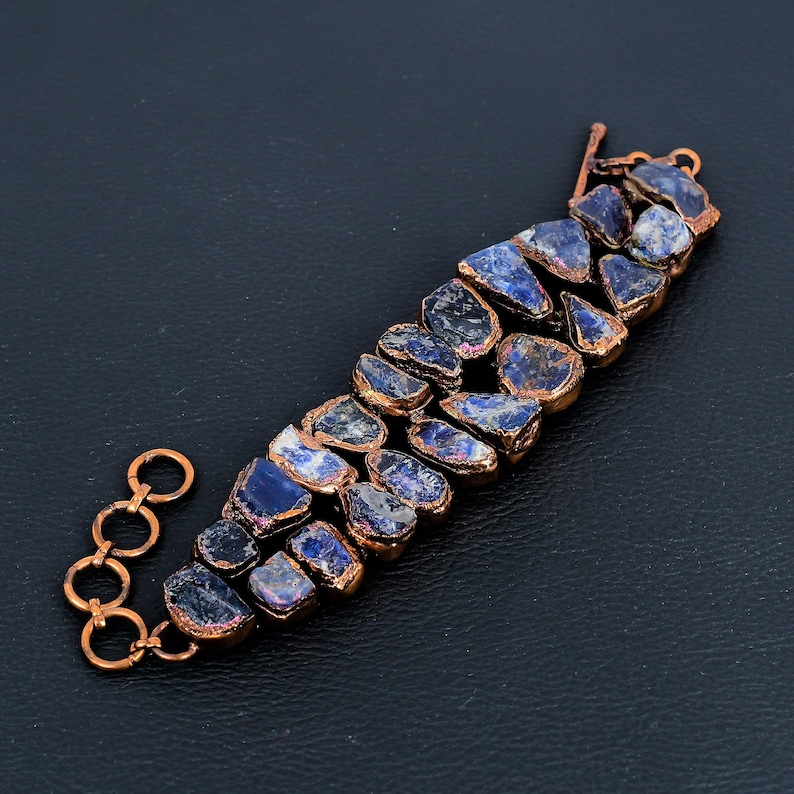 K&ouml;nnte beinhalten: Ein Kupferarmband mit einer Reihe unregelm&auml;&szlig;iger, dunkelblauer und violetter Edelsteine. Das Armband hat einen Kupferverschluss.