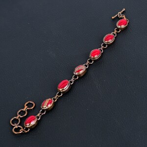 K&ouml;nnte beinhalten: Ein Kupferarmband mit roten ovalen Steinen. Das Armband hat einen Verschluss.