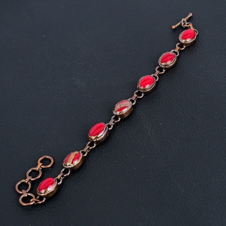 K&ouml;nnte beinhalten: Ein Kupferarmband mit roten ovalen Steinen. Das Armband hat einen Verschluss.