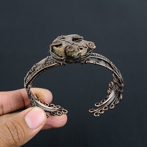 May include: A copper wire wrapped bracelet featuring a fossilized ammonite stone at its centre. The bracelet boasts a delicate, intricate design with numerous loops and swirls.